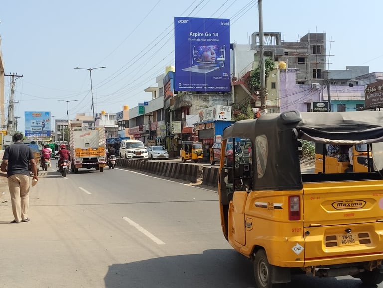 Busy street scene in India with yellow auto-rickshaws, motorcycles, pedestrians, and commercial buildings with blue signage overhead
