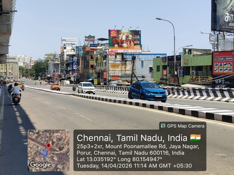 Street view of Chennai showing busy urban road with vehicles, colorful storefronts, and billboards