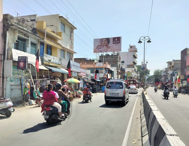 Busy street scene in Indian town with motorcycles, cars, pedestrians, and shops along a wide road under clear sky