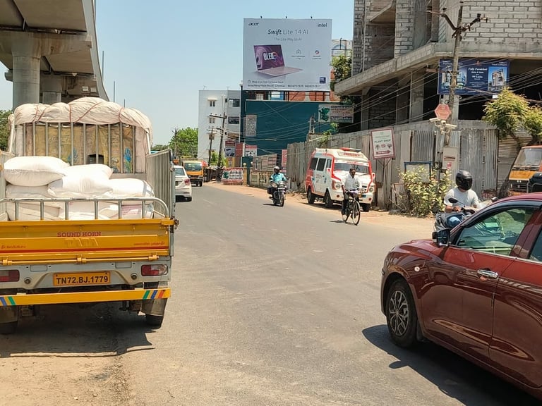 Busy street in India with yellow truck loaded with sacks, red car, motorcycles, and commercial buildings under clear sky