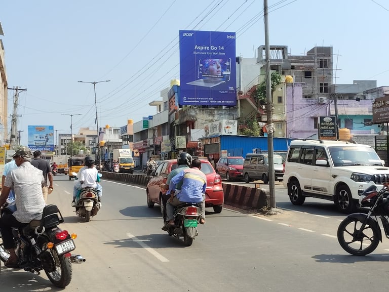 Busy Indian street scene with motorcycles, cars, and pedestrians under advertisements and power lines