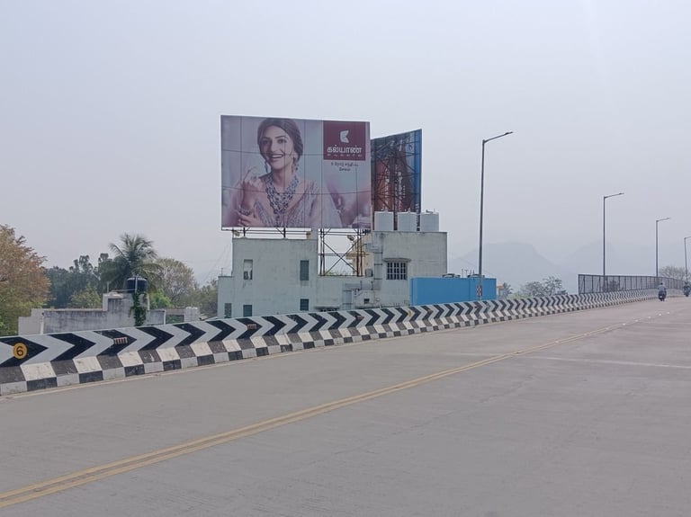 Wide road with black and white striped curbs, buildings, large portrait banner, street lights, and trees under hazy sky