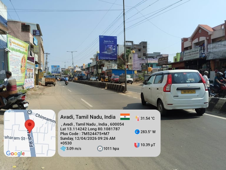 Street scene in Avadi, Tamil Nadu, India showing a white car on a busy commercial road with shops and buildings, Google Maps location overlay visible