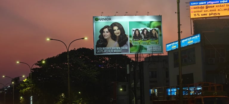 Large illuminated billboard with Garnier advertisements on building at dusk, trees and street lights visible below