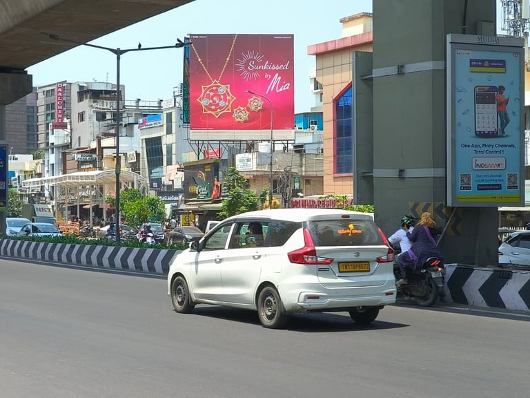 White car driving on urban street with buildings, billboards, and striped road barriers visible in busy Indian city traffic