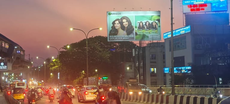 Urban street at dusk with heavy traffic, illuminated billboards overhead, and city buildings silhouetted against a purple sky