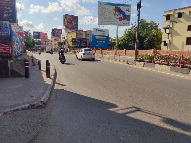 Urban street scene with billboards, vehicles, and buildings under sunny skies in an Indian city