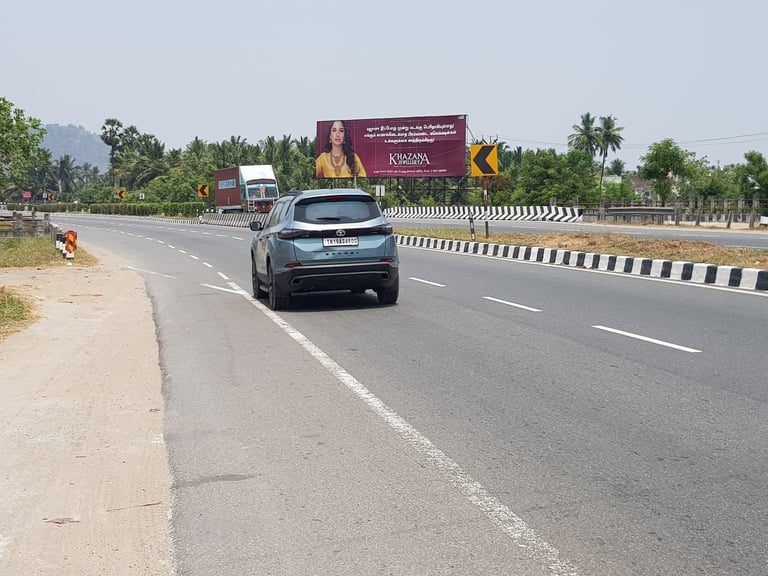 Blue sedan driving on a highway with billboards, trees, and yellow-black striped barriers visible along the roadside