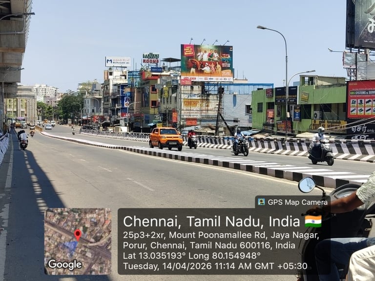 Busy street intersection in Chennai showing traffic, colorful buildings, billboards, and construction vehicles on Mount Poonamallee Road